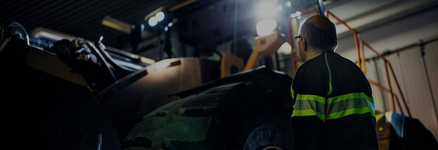 A man looking up at a Volvo wheel loader with its lights on in a darkened room.
